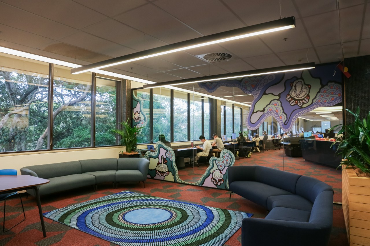 Aboriginal and Torres Strait Islander student space with blue couches and a glass wall featuring elements of Jessie Waratah's artwork Walking on Country.